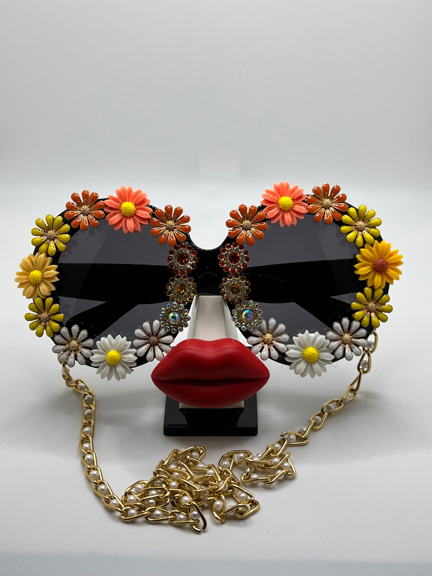 These round, oversized sunglasses have it all - jewels, golden flowers, and daisies in orange, yellow, and white. They're accompanied by an adjustable and removable eyewear chain.