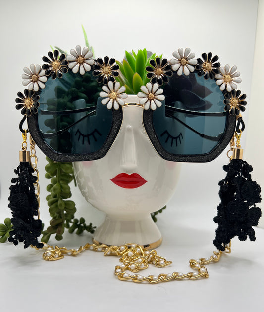 Black and white flowers surround these polygon, square glittering sunglasses and are accompanied by an adjustable and removable eyewear chain and removable lace tassels in black.