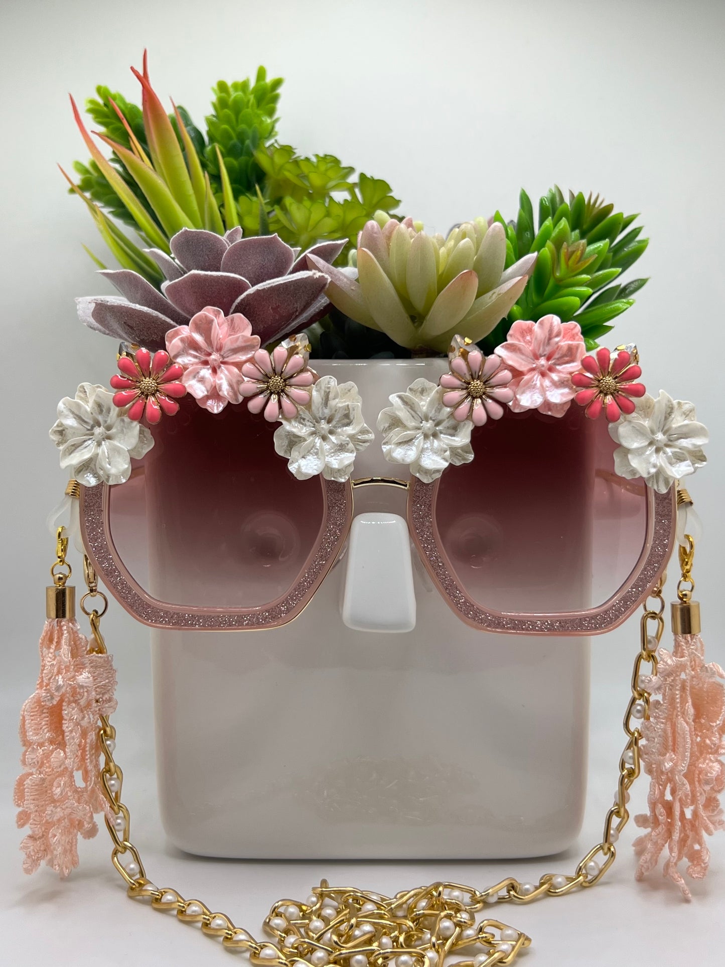 Sparkling rhinestones and pink flowers surround these polygon square sunglasses and are accompanied by an adjustable and removable eyewear chain.