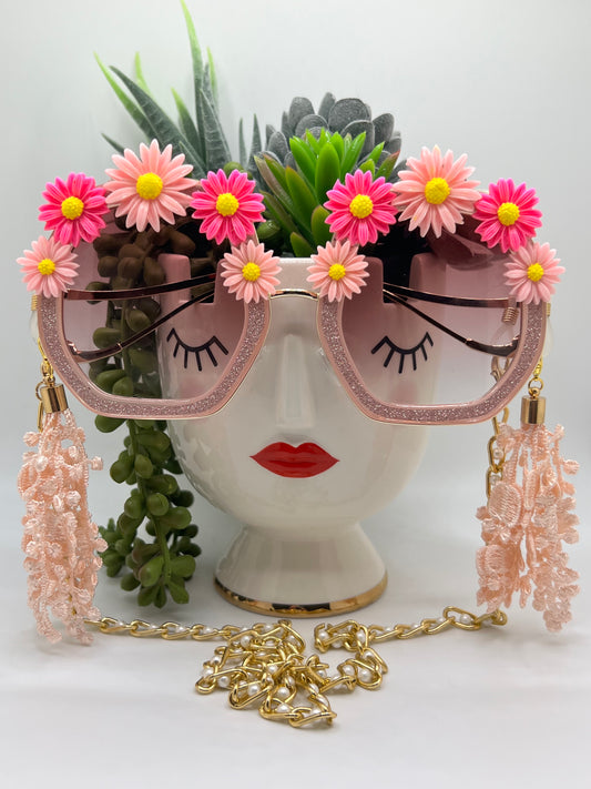 Hues of pink and even pinker sunflowers surround these polygon, glittering pink lenses, and are accompanied by an adjustable and removable eyewear chain and removable lace tassels in pink.