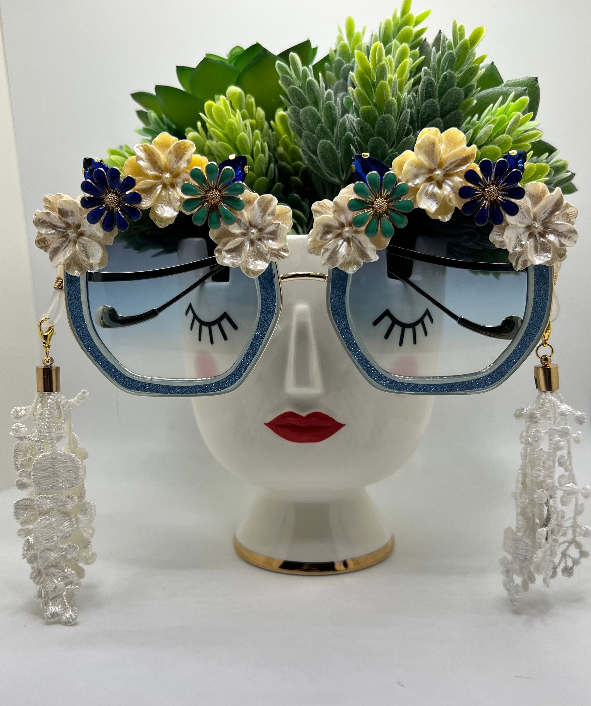 Sparkling rhinestones and blue flowers surround these polygon square sunglasses and are accompanied by an adjustable and removable eyewear chain and lace tassels in white.