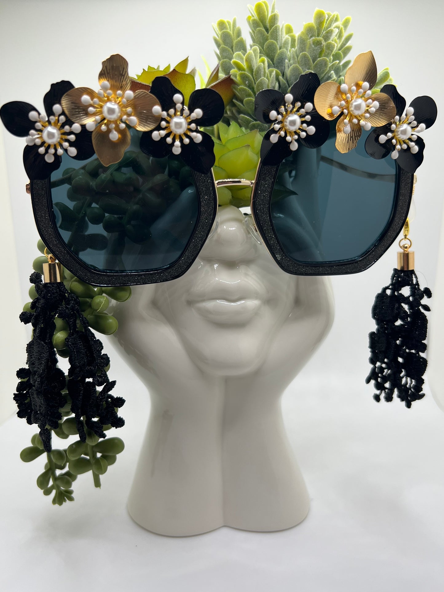 These shimmering black, glitter frames are accented with gold, black, and pearl flowers and come with a removable chain and lace tassels in black.