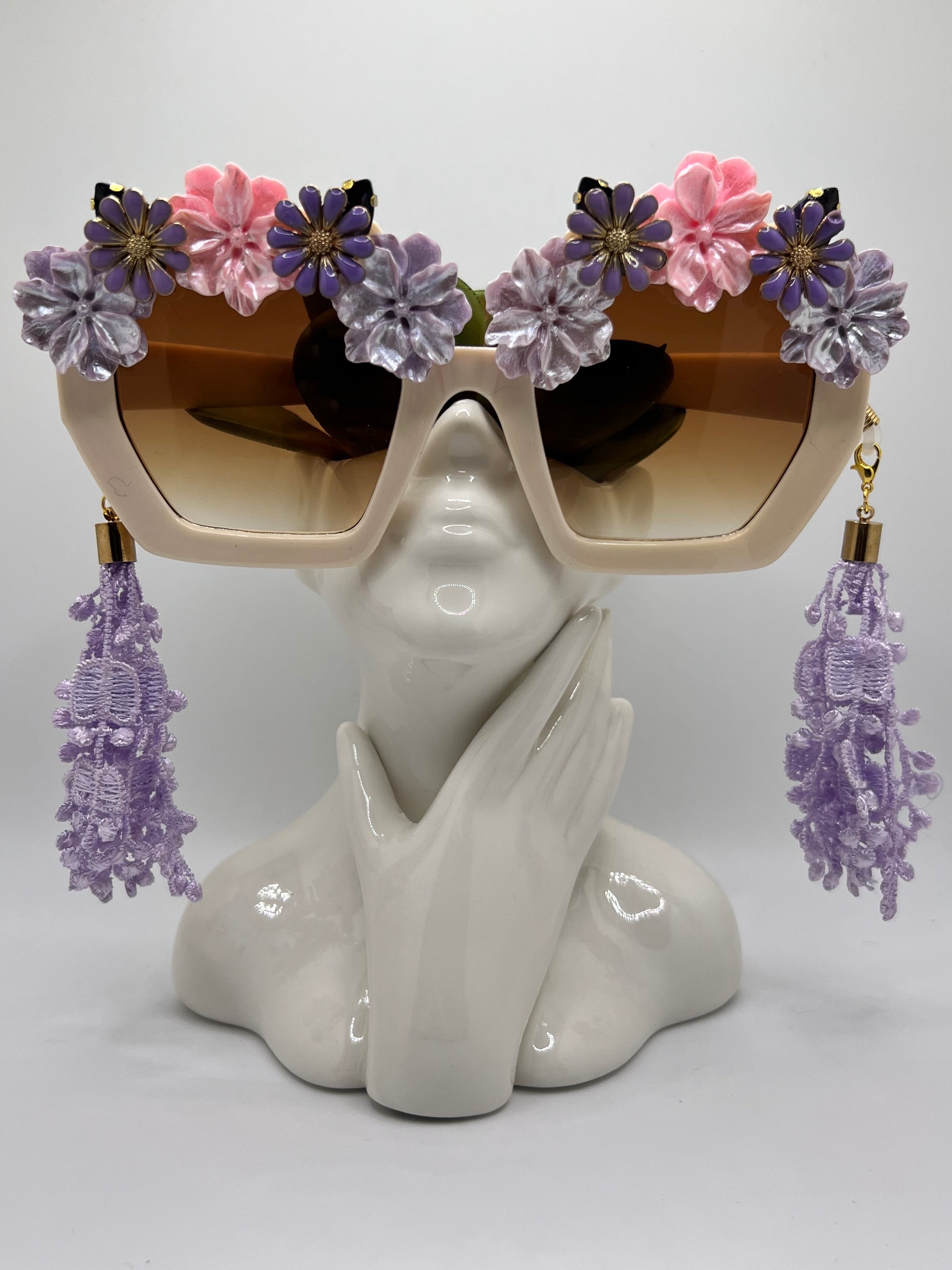 Hues of pink and purple flowers surround these oversized polygon sunglasses and are accompanied by an adjustable and removable eyewear chain and removable lace tassels in purple.