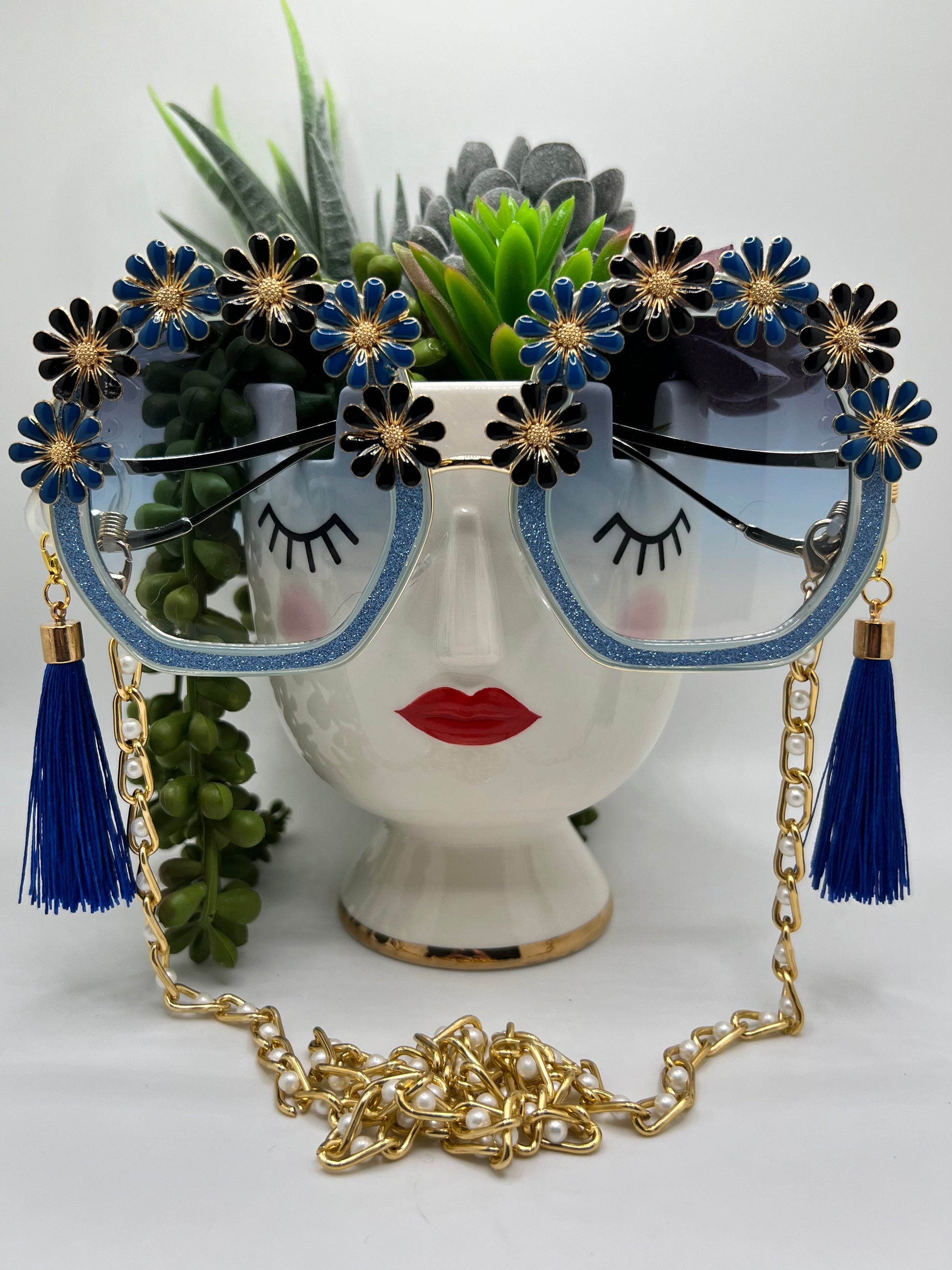 Blue, black, and gold flowers surround these glittering blue frames and are accompanied by an adjustable and removable eyewear chain and removable tassels.