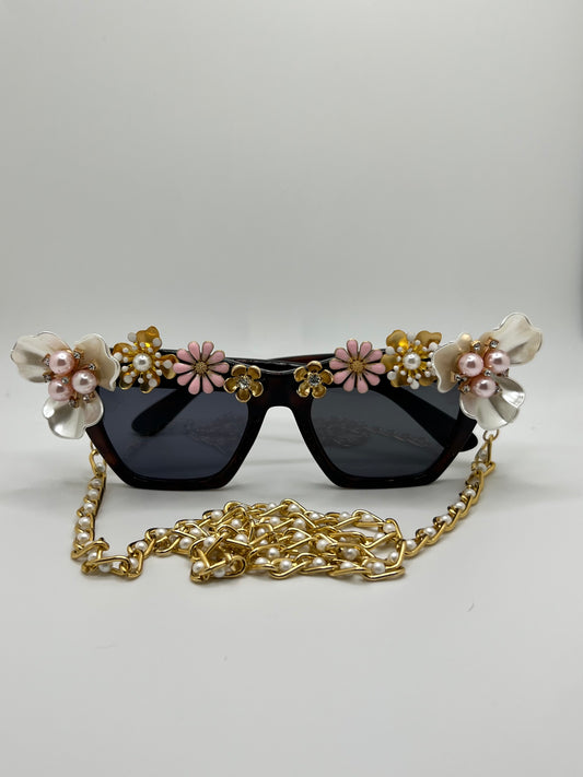 These cat-eye frames in black are embellished with pearl, pink, and gold flowers and come with a gold and pearl, removable chain.