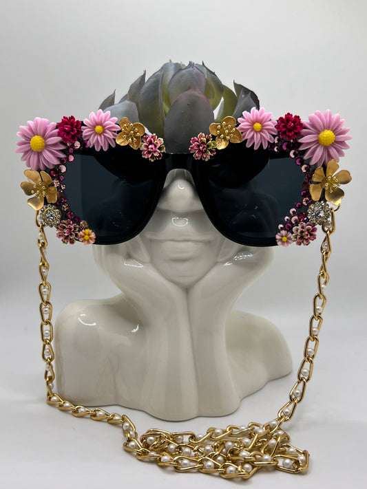 Sparkling gold flowers and bright daisies surround these dark lenses and are accompanied by an adjustable and removable eyewear chain.