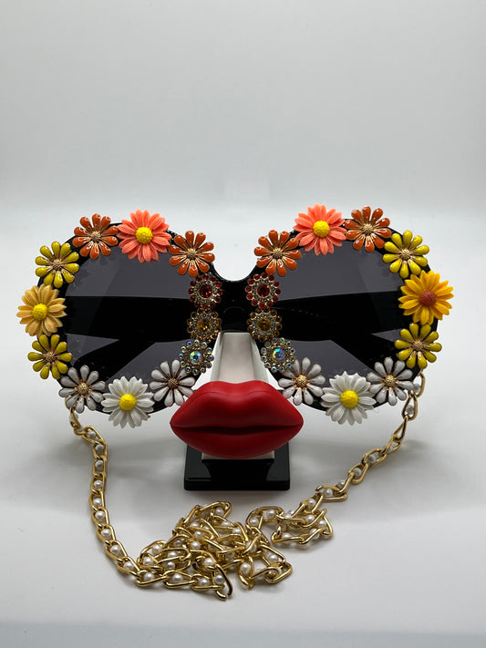 These round, oversized sunglasses have it all - jewels, golden flowers, and daisies in orange, yellow, and white. They're accompanied by an adjustable and removable eyewear chain.