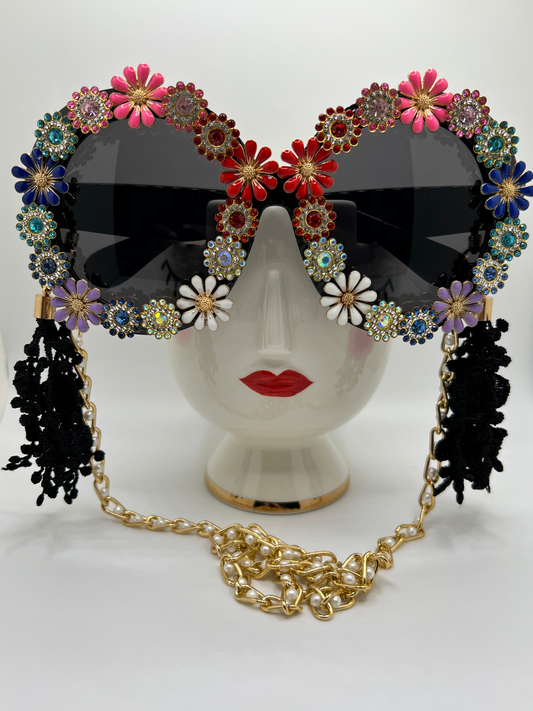 These round, oversized sunglasses have it all - jewels, flowers, and rainbows, and are accompanied by an adjustable and removable eyewear chain and removable lace tassels in black.