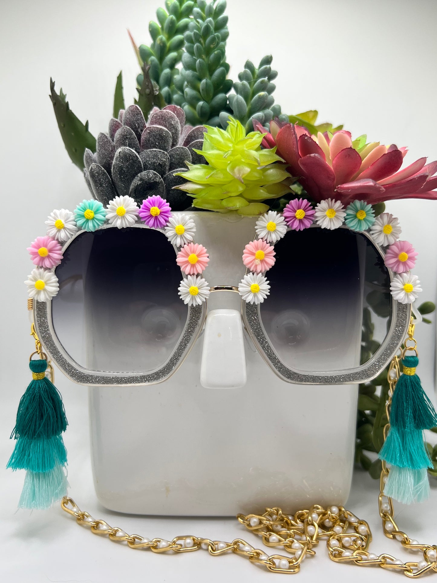 These oversized, octagonal glasses are covered in pastel daisy embellishments and oversized, removable tassels and come with a removable chain.