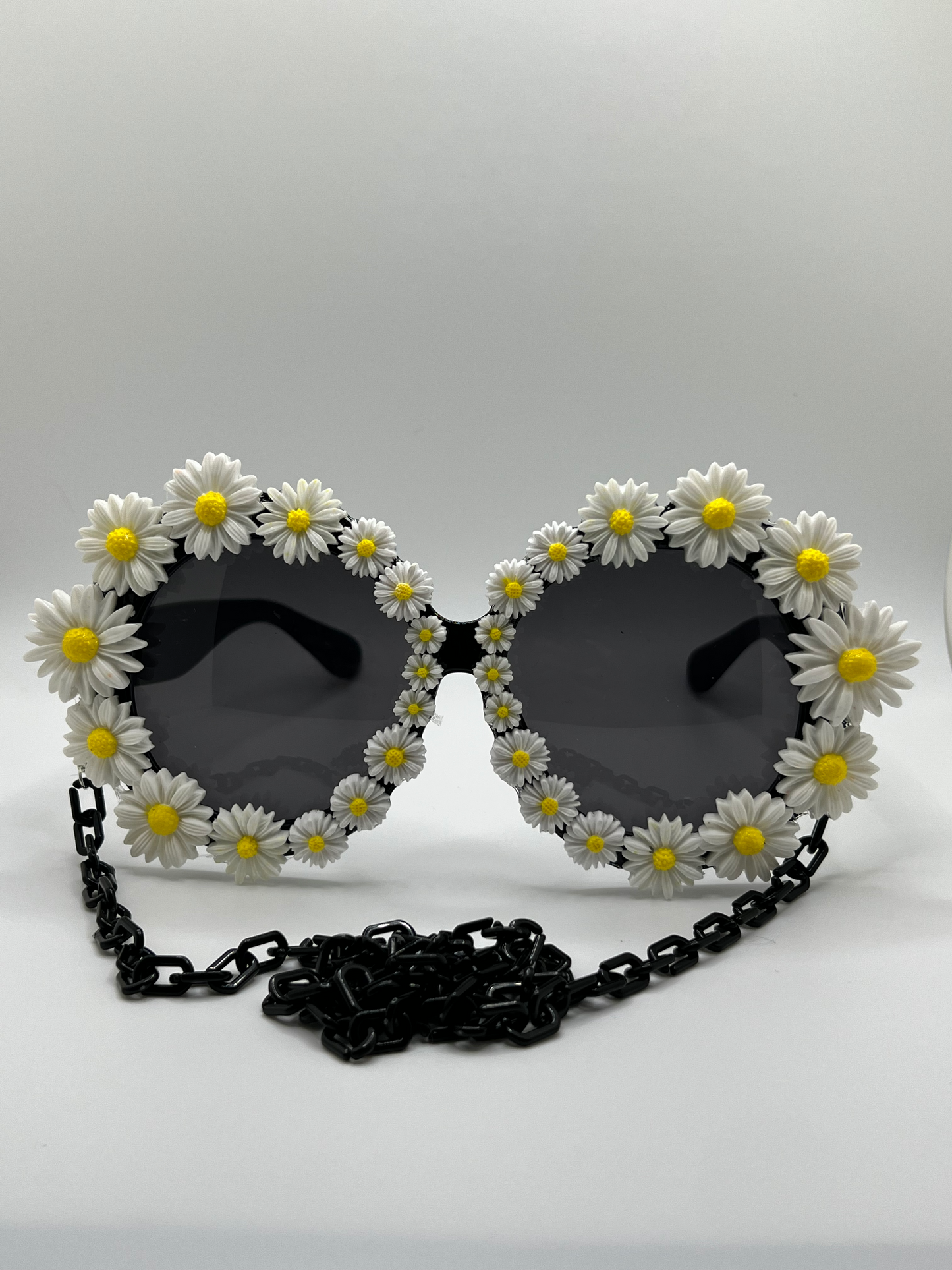 Dozens of white daisies surround these round, oversized sunglasses and are accompanied by an adjustable and removable eyewear chain.